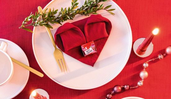 Gefaltetes Herz aus einer roten Serviette, das auf einem Teller liegt.