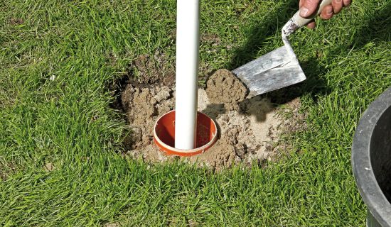 Mann betoniert Pfosten in den Boden