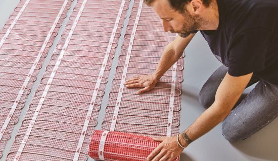 Mann verlegt elektrische Fußbodenheizung im Badezimmer