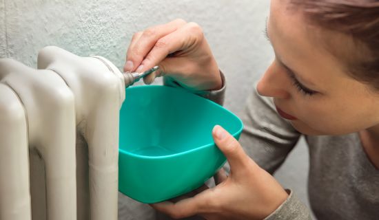 Frau entlüftet einen Heizkörper mithilfe eines Schlüssels