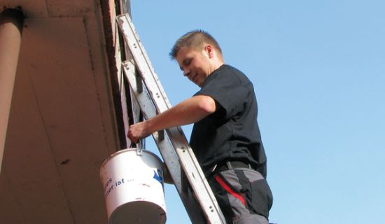 Mann steht auf Leiter, die an den Balkon gelehnt ist