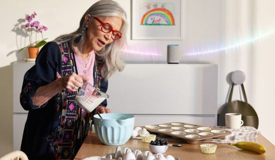 Alte Frau backt, im Hintergrund der Sprachassistent