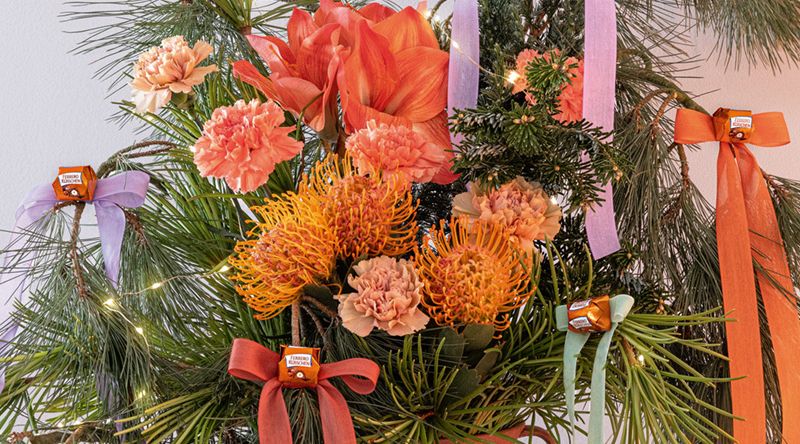 Festlicher Blumenstrauß mit Schleifen. Zu sehen sind Eukalyptus, Amaryllis, Nelken, Nadelkissen-Protea, Seidenkiefer, Schirmtanne in einem Strauß mit dekorativen Schleifenbändern.