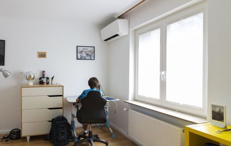 Junge sitzt im Arbeitszimmer, über ihm ist eine Klimaanlage installiert