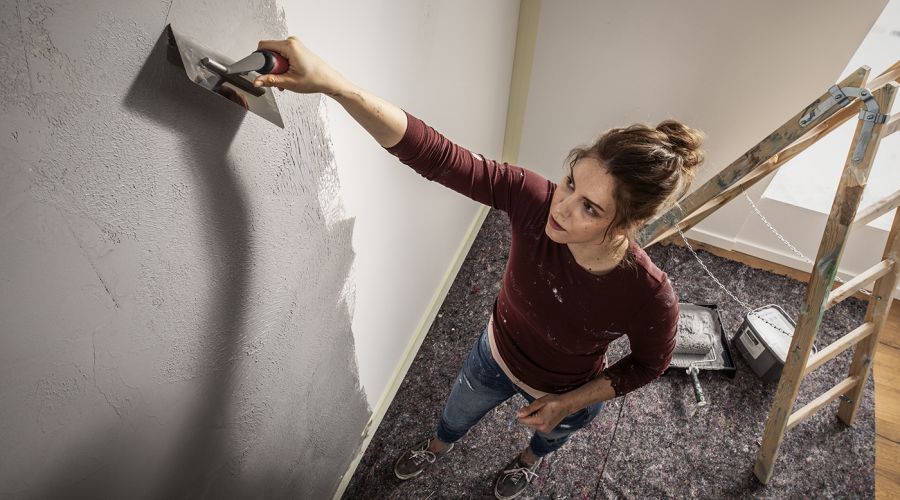 Eine Frau trägt mit einer Kelle Putz auf eine Wand auf