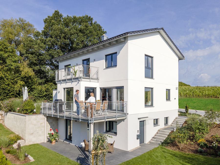 Haus in Hanglage, auf dem Balkon steht ein Ehepaar