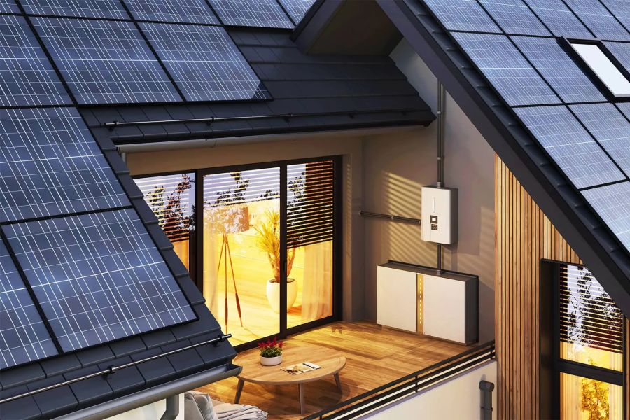 An der Außenwand eines modernen Hauses mit Solaranlage ist auf einem Holzbalkon ein weißer Batteriespeicher montiert.