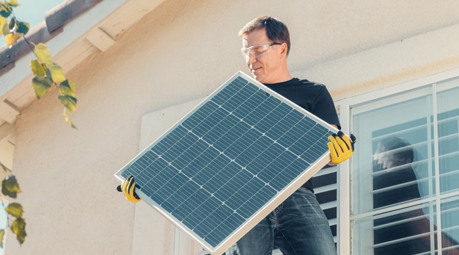 Mann trägt Solarpanel aufs Haus