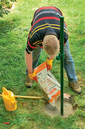 Mann füllt das Loch mit dem Pfosten mit Beton auf