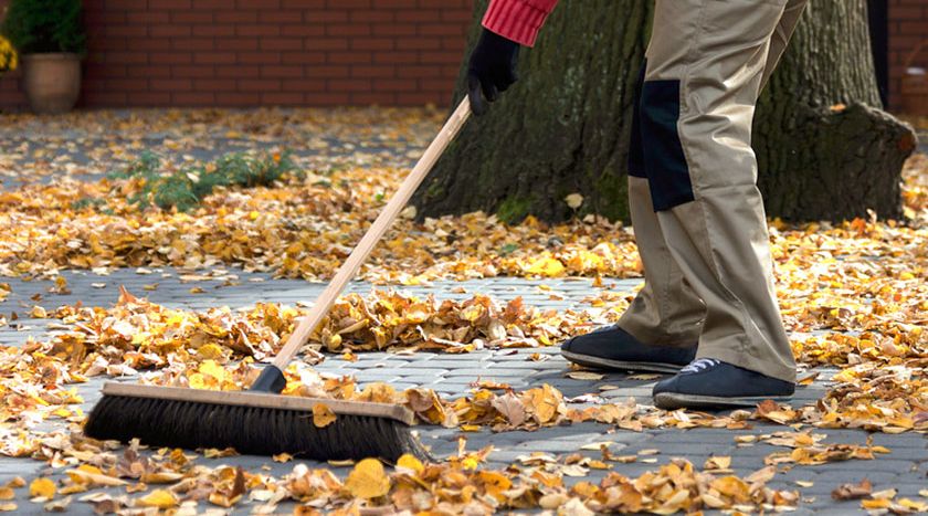 Mann fegt Herbstlaub zusammen