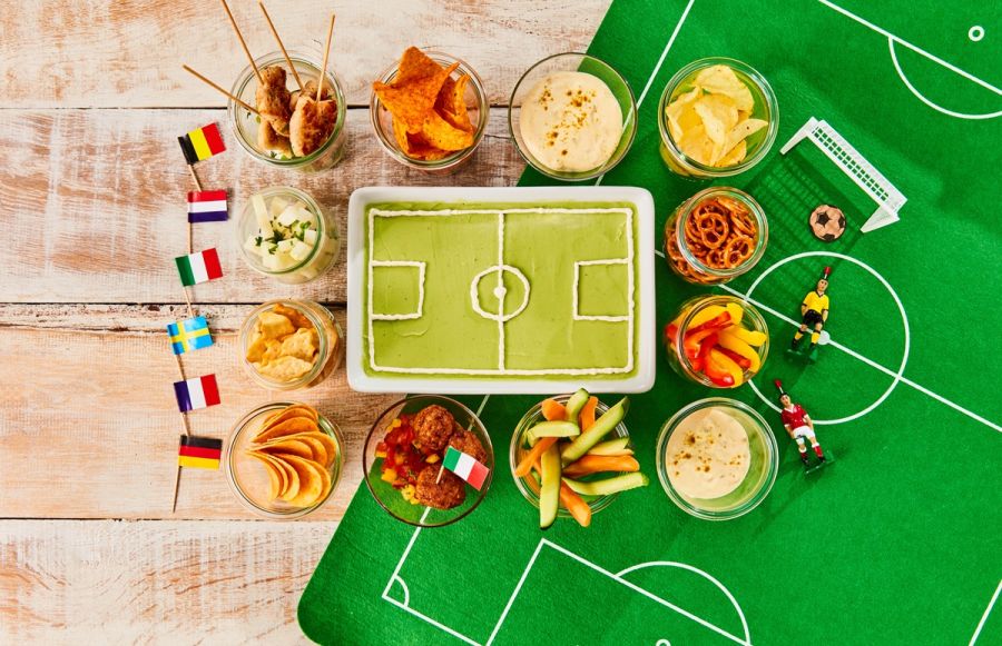 Kuchen in Form eines Fußballstadions, darum sind Snacks gruppiert