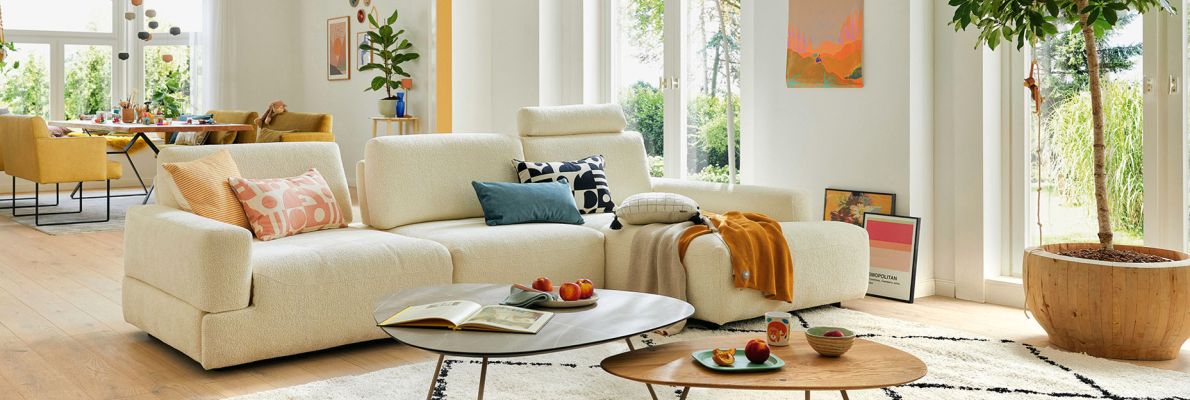 Wohnzimmerambiente in hellen Farbtönen mit großem Sofa, Beistelltischen, Stehleuchte.