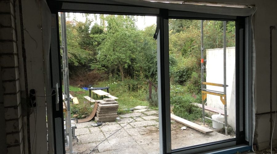 Blick aus dem Haus in den Garten, draußen liegen noch lose Terrassenplatten und ein etwas verwildert wirkender Garten.