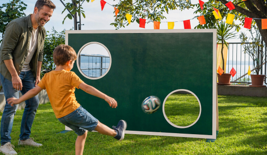 Kind schießt auf eine Torwand, der Vater schaut begeistert zu