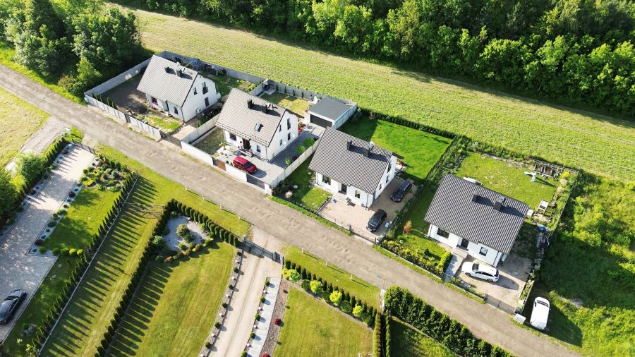Die Vogelperspektive zeigt mehrere Einfamilienhäuser, die auf länglichen Grundstücken gebaut sind. Eine schmale Zufahrtsstraße führt an den vorderen Grundstücken vorbei zu den weiter hinten liegenden Häusern. Dies illustriert die typische bauliche Situati