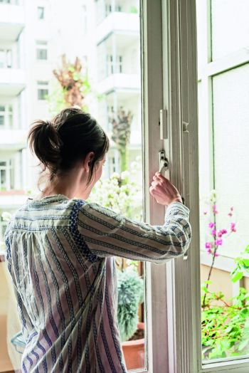 Frau schließt Fenster, an dem Fensterkontakte als Einbruchschutz montiert sind