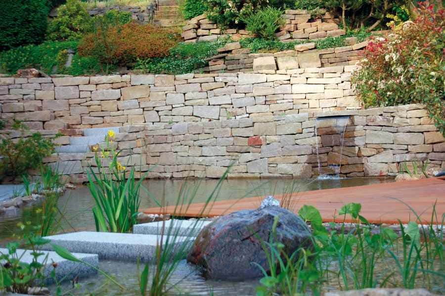 Schwimmteich mit Natursteinmauer am Hang
