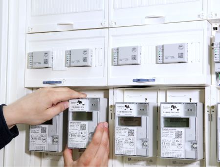 Detailaufnahme einer Hand, die einen modernen digitalen Stromzähler in einem weißen Schaltschrank bedient. Über den Zählern sind Smart Meter Gateways montiert, die für die verschlüsselte Übertragung der Messdaten zuständig sind.