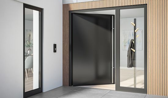 Das Bild zeigt einen modernen Eingangsbereich mit einer großen, schwarzen Tür, die weit geöffnet ist. Die Türschwelle ist flach. Links befindet sich ein schmaler Fensterbereich, während rechts eine Garderobe mit einem hängenden Mantel sichtbar ist.