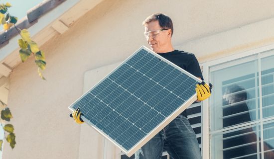 Mann trägt Solarpanel aufs Haus