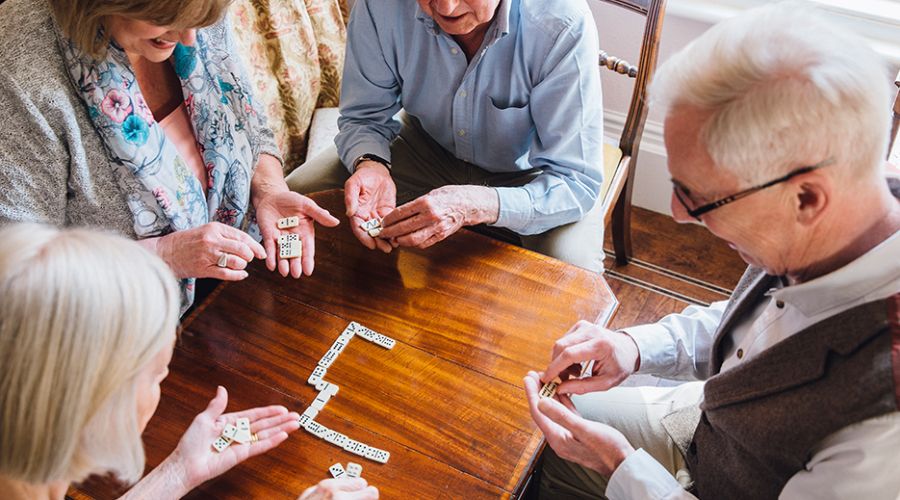 Vier Senioren sitzen gemeinsam an einem Tisch und spielen Domino.