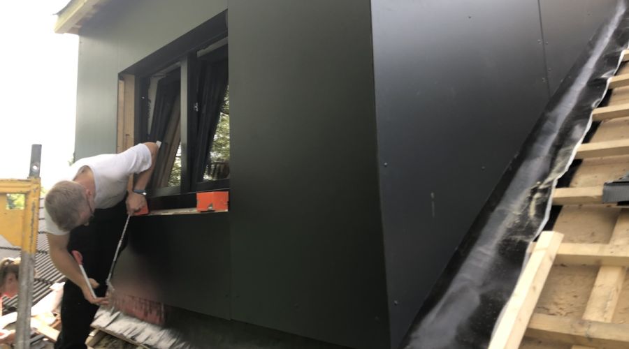 Handwerker nimmt Maßarbeiten an einer schwarz verblendeten Gaube vor.