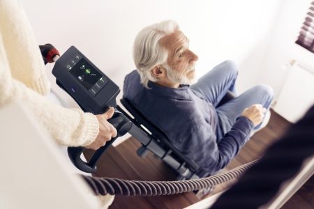 Nahaufnahme: Ein älterer Mann sitzt in einem Treppensteiger, während eine Person das digitale Bedienfeld des Geräts bedient.