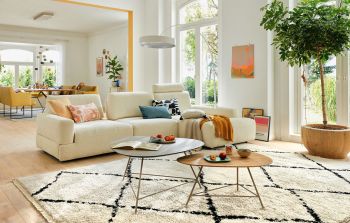 Wohnzimmerambiente in hellen Farbtönen mit großem Sofa, Beistelltischen, Stehleuchte.