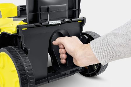 Das Bild zeigt die Detailaufnahme eines Rasenmähers in Gelb und Schwarz, bei dem eine Hand das Mulchkit öffnet. Der Hintergrund ist hell und neutral, wodurch der Fokus auf dem Gerät liegt. Die Szene wirkt sachlich und vermittelt einen Eindruck von Funktio