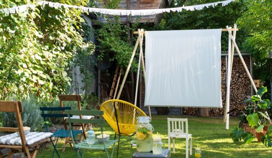 In einem Garten steht eine aufgebaute Leinwand aus einem Bettlaken, davor stehen Stühle