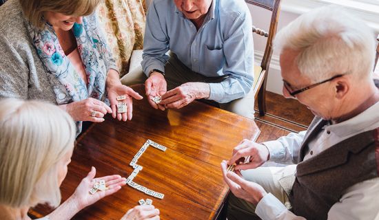 Vier Senioren sitzen gemeinsam an einem Tisch und spielen Domino.