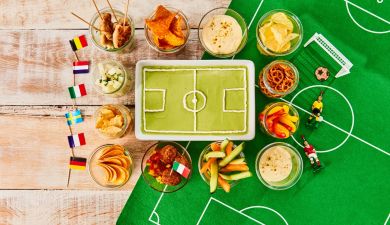 Kuchen in Form eines Fußballstadions, darum sind Snacks gruppiert