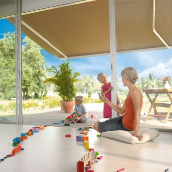 Eine Frau sitzt mit ihren Kindern unter einer aufgespannten Markise auf der Terrasse