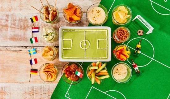 Kuchen in Form eines Fußballstadions, darum sind Snacks gruppiert