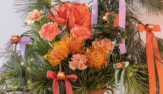 Festlicher Blumenstrauß mit Schleifen. Zu sehen sind Eukalyptus, Amaryllis, Nelken, Nadelkissen-Protea, Seidenkiefer, Schirmtanne in einem Strauß mit dekorativen Schleifenbändern.