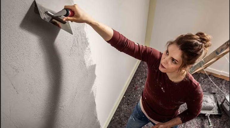 Eine Frau trägt mit einer Kelle Putz auf eine Wand auf