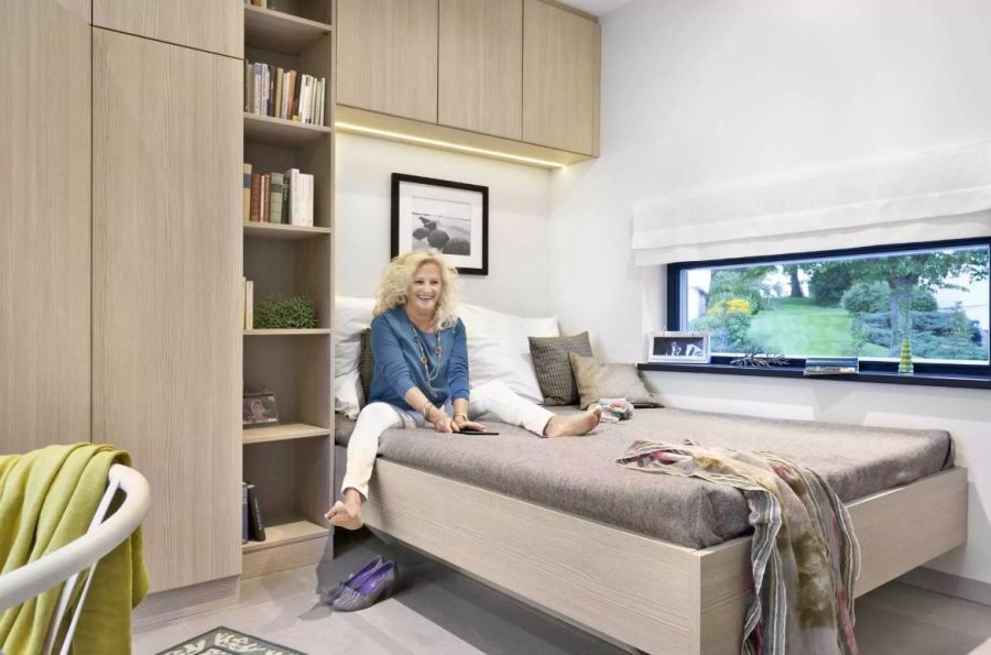 Frau sitzt auf ihrem Bett, darüber befindet sich eine Einbauschrank