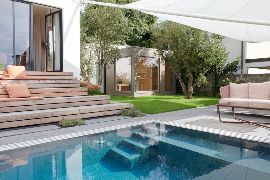 Modernes Saunahaus mit großen Glasfronten in einem Garten mit Swimmingpool, Terrasse und Sitzbereich.