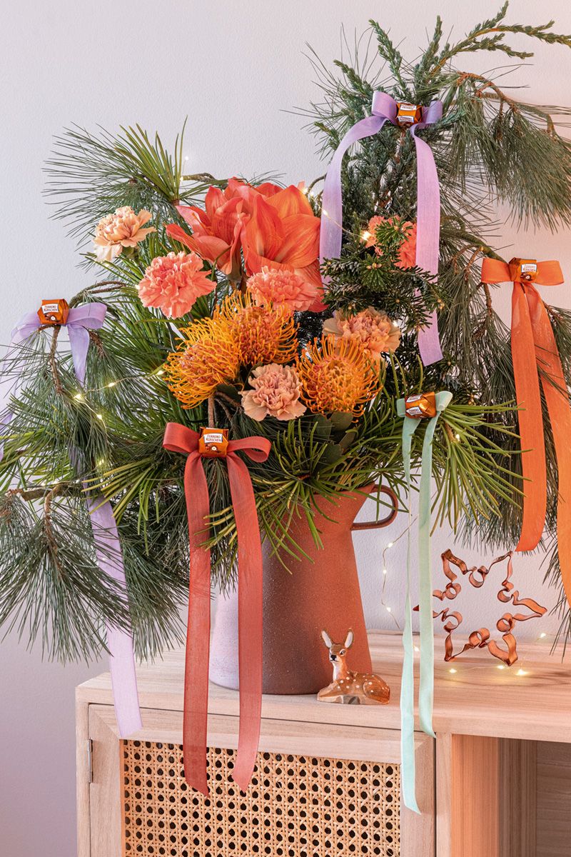 Festlicher Blumenstrauß mit Schleifen. Zu sehen sind Eukalyptus, Amaryllis, Nelken, Nadelkissen-Protea, Seidenkiefer, Schirmtanne in einem Strauß mit dekorativen Schleifenbändern.