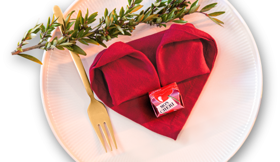 Gefaltetes Herz aus einer roten Serviette, das auf einem Teller liegt.