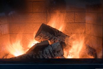 Nahaufnahme eines Kaminfeuers mit brennendem Holz, die Flammen lodern intensiv vor einem gemauerten Hintergrund.
