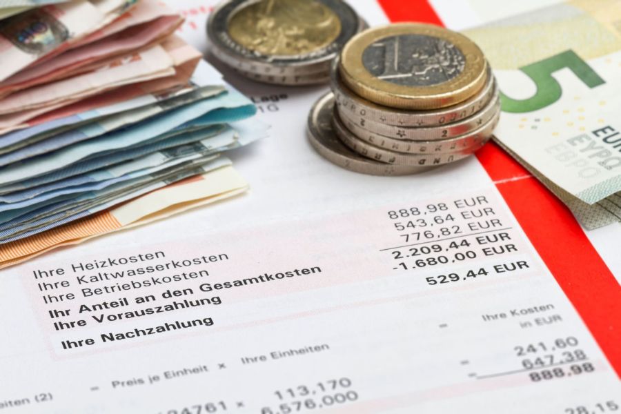 Eine detaillierte Nebenkostenabrechnung mit Euro-Geldscheinen und Münzen, auf der die Zeilen Heizkosten, Betriebskosten und Nachzahlung gedruckt sind.