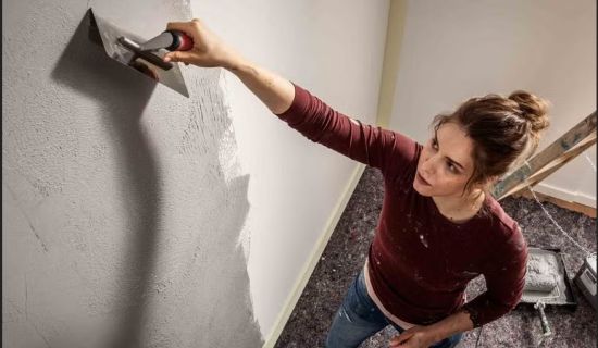 Eine Frau trägt mit einer Kelle Putz auf eine Wand auf