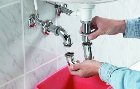 Mann nimmt Rohr unterm Waschbecken ab