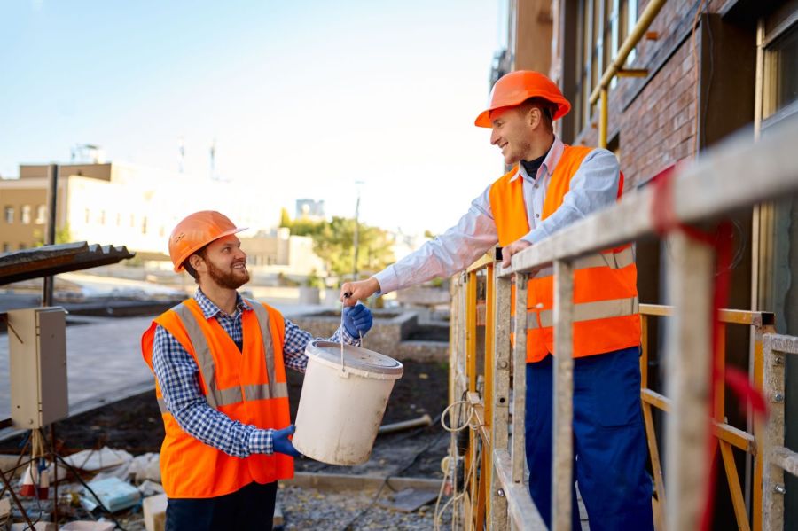 Zwei Bauhelfer reichen sich einen Eimer auf der Baustelle