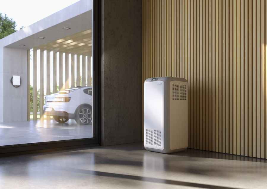 Ein moderner, weißer SENEC-Heimspeicher steht in einem Wohnraum. Durch ein großes Fenster ist im Hintergrund ein in einer Garage geparktes Elektroauto zu sehen.