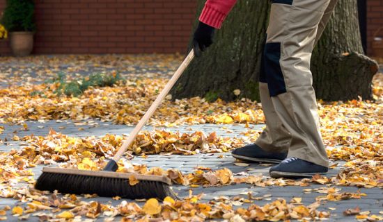 Mann fegt Herbstlaub zusammen