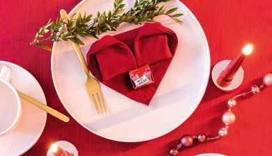 Gefaltetes Herz aus einer roten Serviette, das auf einem Teller liegt.
