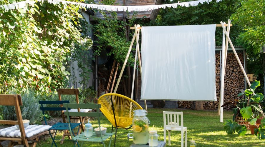 In einem Garten steht eine aufgebaute Leinwand aus einem Bettlaken, davor stehen Stühle