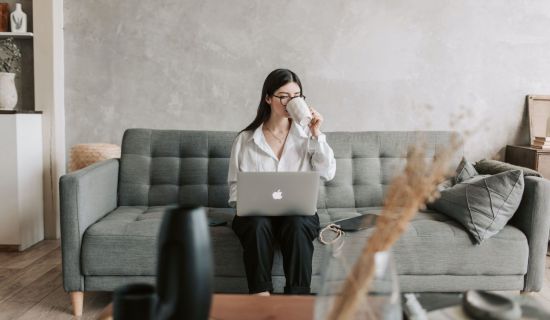 Frau sitzt mit einem Laptop auf einer Couch